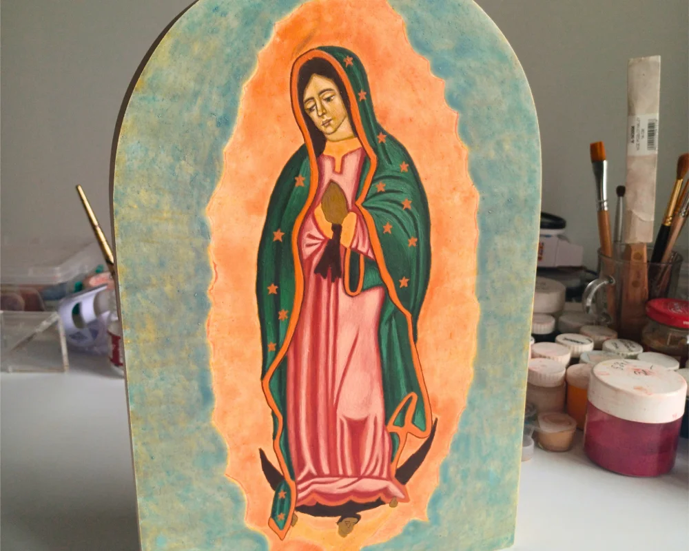 Hand-painted Our Lady of Guadalupe icon on wood panel with tools in background.