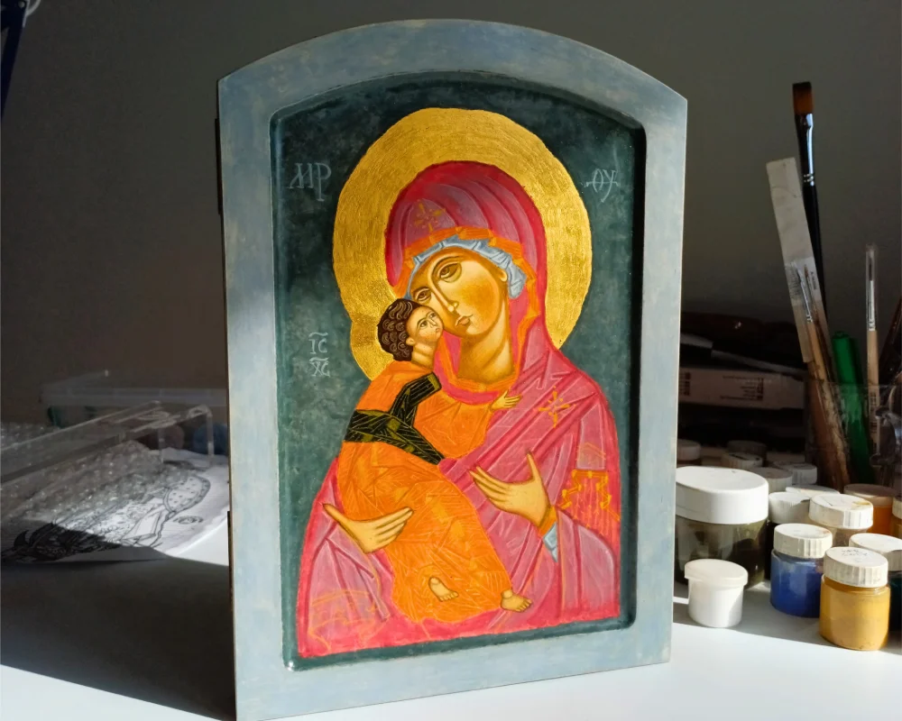 Hand-painted Our Lady of Vladimir icon in an iconography studio, surrounded by professional brushes and egg tempera pigments.